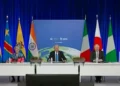World leaders sit at a large conference table on a stage with flags of various countries in the background, during an international summit with blue curtains. The discussion prominently features the Renewable energy transition and key COP summit outcomes.