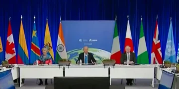 World leaders sit at a large conference table on a stage with flags of various countries in the background, during an international summit with blue curtains. The discussion prominently features the Renewable energy transition and key COP summit outcomes.
