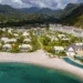 An aerial view of a beachfront resort in St. Vincent and the Grenadines, showcasing multiple buildings, a pool, and sandy beach surrounded by lush, green mountains and turquoise water—a true gem of Caribbean luxury travel.