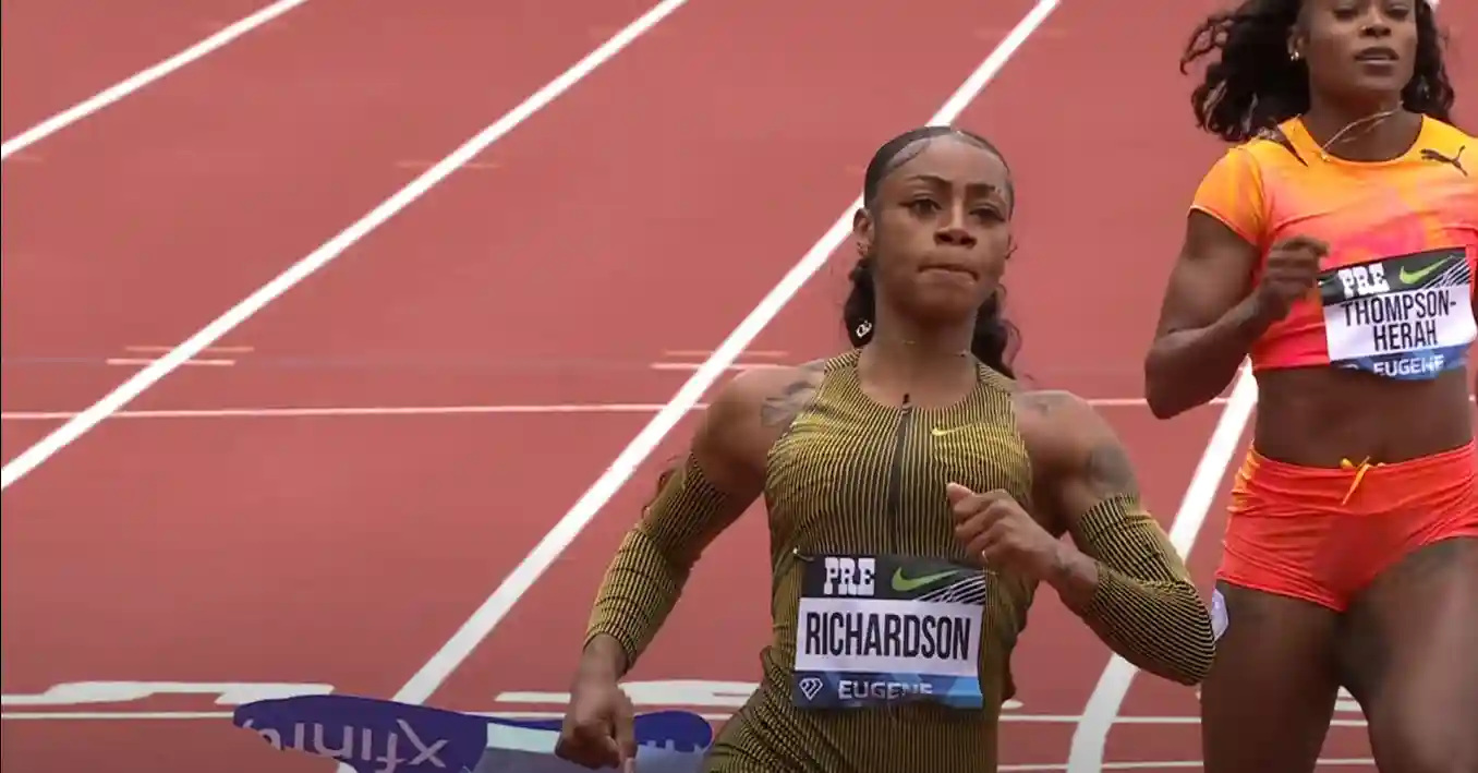 Two athletes are running on a track. The athlete in the foreground, Sha'Carri Richardson, wears a green uniform with "RICHARDSON" on it. Competing in the renowned Prefontaine Classic, the athlete behind wears an orange uniform with "THOMPSON-HERAH" emblazoned across it.