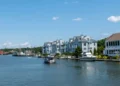 A calm river with boats docked along the shore is lined with various waterfront houses and buildings under a clear blue sky. Governor Ned Lamont's proactive stance on renewable energy in Connecticut ensures that this serene landscape remains protected as we look toward climate action 2024.