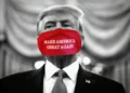 A man in a suit wearing a red face mask with the words "MAKE AMERICA GREAT AGAIN" printed on it stands against a blurred, monochromatic background. The scene evokes the heightened tensions surrounding the Trump hush money guilty verdict in his historic trial.