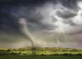 A tornado touches down in a rural landscape under a stormy summer sky with lightning, showcasing a dramatic weather event.