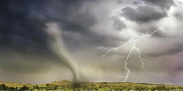 A tornado touches down in a rural landscape under a stormy summer sky with lightning, showcasing a dramatic weather event.