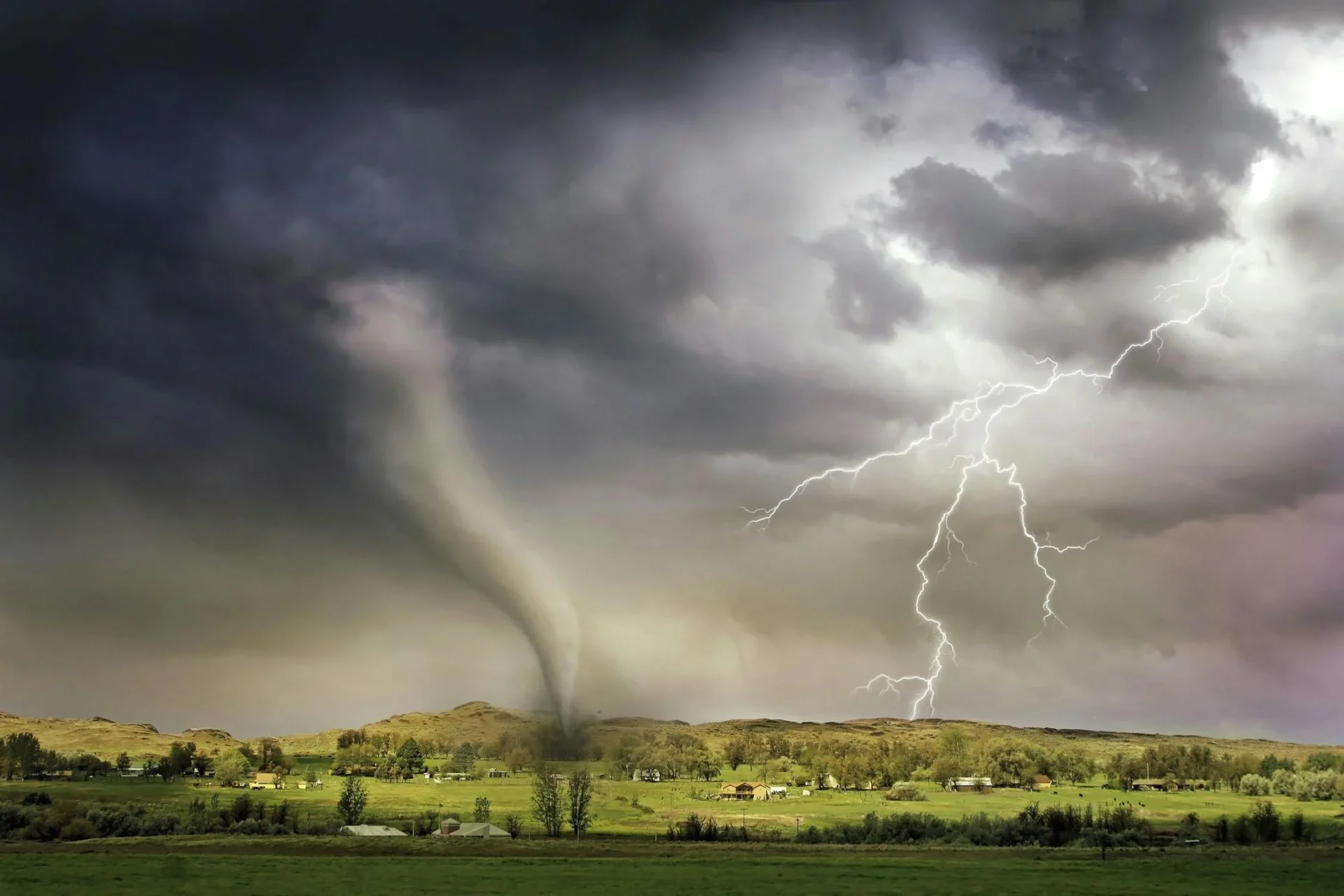 A tornado touches down in a rural landscape under a stormy summer sky with lightning, showcasing a dramatic weather event.