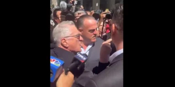 Robert De Niro in A crowd of camera operators and reporters surround two men in suits outdoors, with microphones visible in the foreground.