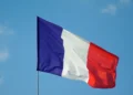 The French flag, featuring vertical stripes of blue, white, and red, is waving against a clear blue sky in a strong stance of anti-terrorism.