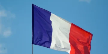 The French flag, featuring vertical stripes of blue, white, and red, is waving against a clear blue sky in a strong stance of anti-terrorism.