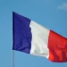The French flag, featuring vertical stripes of blue, white, and red, is waving against a clear blue sky in a strong stance of anti-terrorism.
