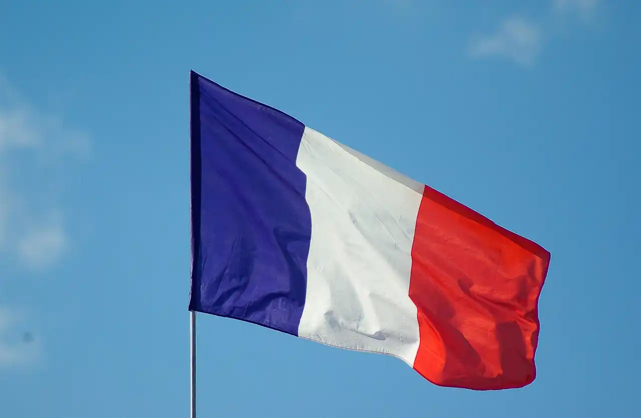 The French flag, featuring vertical stripes of blue, white, and red, is waving against a clear blue sky in a strong stance of anti-terrorism.