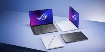 A collection of four laptops on a light blue surface. Two are open, one facing forward and the other at an angle, displaying colorful screens with a logo. Among them is the high-end gaming ASUS ROG Zephyrus G16. Two laptops are closed, one white and one black.