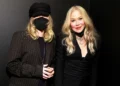 Two women with long blonde hair stand next to each other. One wears a black hat and face mask, while the other, who resembles Christina Applegate, is dressed in black with several necklaces. Both are smiling, seemingly carefree despite one’s daughter diagnosed with POTS.