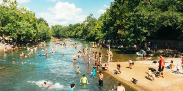 A large crowd of people swim and gather around a natural waterway in Connecticut, surrounded by trees on a sunny June 18-23, 2024, basking in the extreme hot weather.
