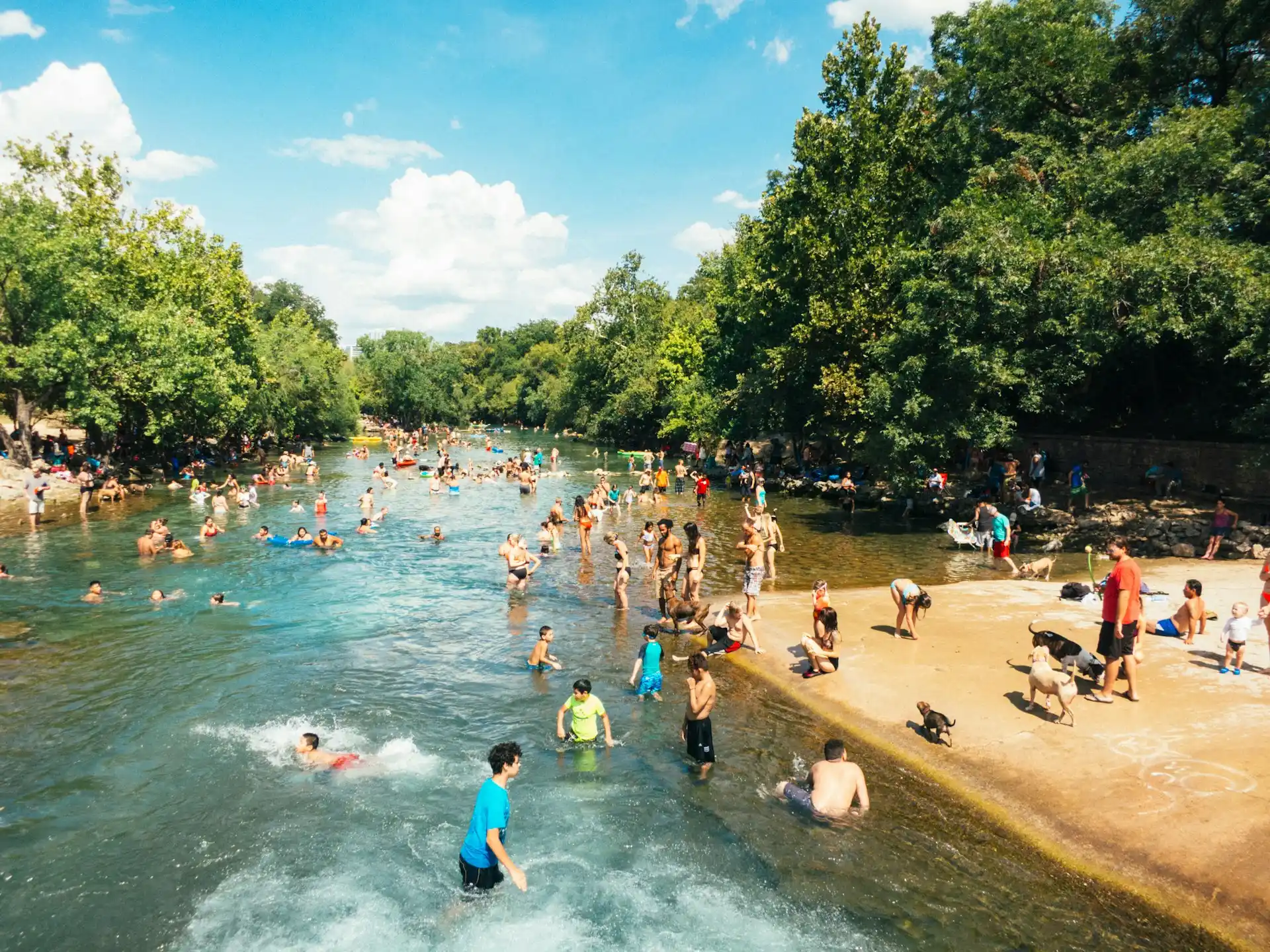 A large crowd of people swim and gather around a natural waterway in Connecticut, surrounded by trees on a sunny June 18-23, 2024, basking in the extreme hot weather.