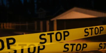 Yellow "STOP" tape cordons off an area in front of a house at night, casting a somber pall over the neighborhood as trees and other structures loom in the background—marking the site of a recent oven tragedy in Kansas City.