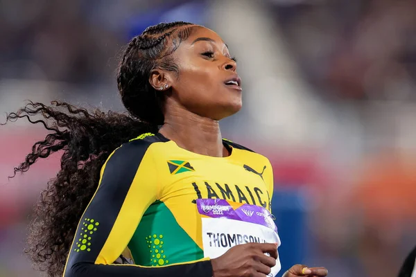Elaine Thompson-Herah in a green, yellow, and black uniform, injured after competing in a sprinting event at the New York Grand Prix, with a visible Jamaican flag and 'Jamaica' written on her outfit.