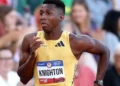 A male athlete, Erriyon Knighton, wearing a yellow racing outfit with the name "Knighton" and number "1" displayed on his chest, runs on a track during a race as part of the U.S. Olympic Team, achieving an impressive 19.77-second finish.