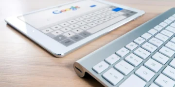 A white tablet displaying the Google search page is placed on a wooden surface next to a slim, silver wireless keyboard, highlighting the seamless integration enabled by the strategic partnership between Google Cloud and Oracle Database.
