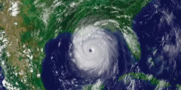 A satellite image of Hurricane Beryl forming over the Gulf of Mexico shows a well-defined eye and spiral cloud bands extending outward. The surrounding land along the Gulf Coast and ocean areas are visible, providing critical updates on this powerful storm.
