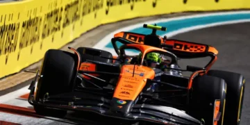 A Formula 1 car with an orange and black livery is speeding on a race track during the F1 Spanish GP 2024, surrounded by yellow advertising banners. The driver, potentially Lando Norris aiming for pole position, is focused, and the background includes a crowd in the stands enjoying the Spanish Grand Prix highlights.