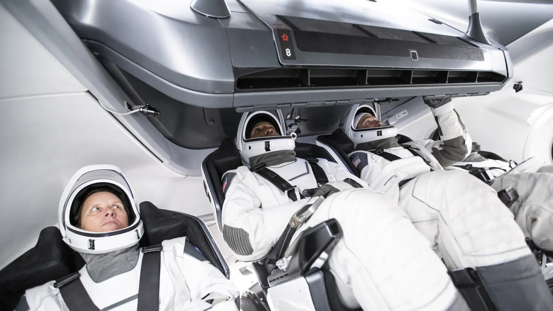 Three astronauts in white spacesuits are seated and secured inside a modern NASA spacecraft, equipped with advanced technology. This deorbit vehicle ensures their safe return from space.