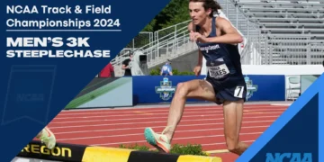 Athlete Parker Stokes, in a blue uniform, competes in the Men's 3,000m Steeplechase event at the NCAA Track & Field Championships 2024, leaping over a barrier on the track.