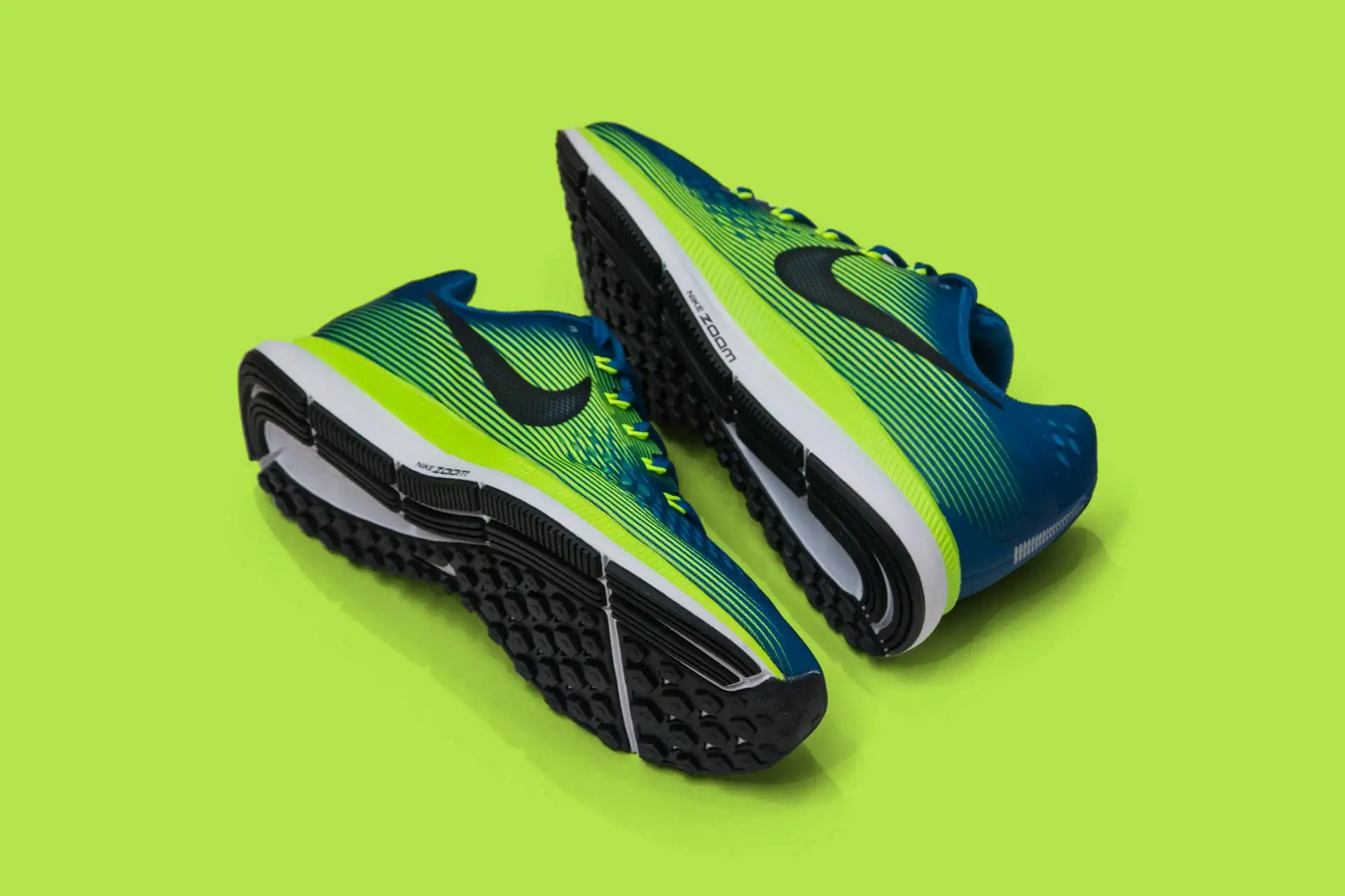 Image of a pair of blue and green athletic running shoes with black soles, placed on a bright green background, showcasing the innovative design that Nike CEO John Donahoe praised for its blend of style and performance.