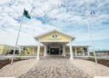 A yellow building with white columns labeled "Odyssey Aviation Exuma," flanked by two flagpoles, one with the Bahamian flag and one with the "Odyssey Aviation" flag, stands proudly under a partly cloudy sky, illustrating the charm of Caribbean infrastructure.