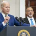 A man in a blue suit speaks at a podium with the presidential seal, addressing the Israel-Hamas ceasefire, while another man in a suit and tie stands behind him in a room with a U.S. flag and bookshelf.