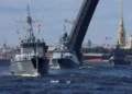 Naval ships pass under an open drawbridge on a river, with a backdrop of historical buildings and a golden spire, reminiscent of scenes featuring Russian warships in Cuba news 2024.