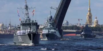 Naval ships pass under an open drawbridge on a river, with a backdrop of historical buildings and a golden spire, reminiscent of scenes featuring Russian warships in Cuba news 2024.