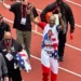 A man wearing a patriotic outfit with a graphic of Snoop Dogg on it is walking on the track, smiling, and giving thumbs up during the Olympic Trials 200m event. He is surrounded by several other people.