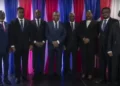A group of eleven people in formal attire stands in front of red, white, and blue striped curtains, posing for a photo to mark Haiti's new government formation.