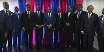 A group of eleven people in formal attire stands in front of red, white, and blue striped curtains, posing for a photo to mark Haiti's new government formation.