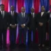 A group of eleven people in formal attire stands in front of red, white, and blue striped curtains, posing for a photo to mark Haiti's new government formation.