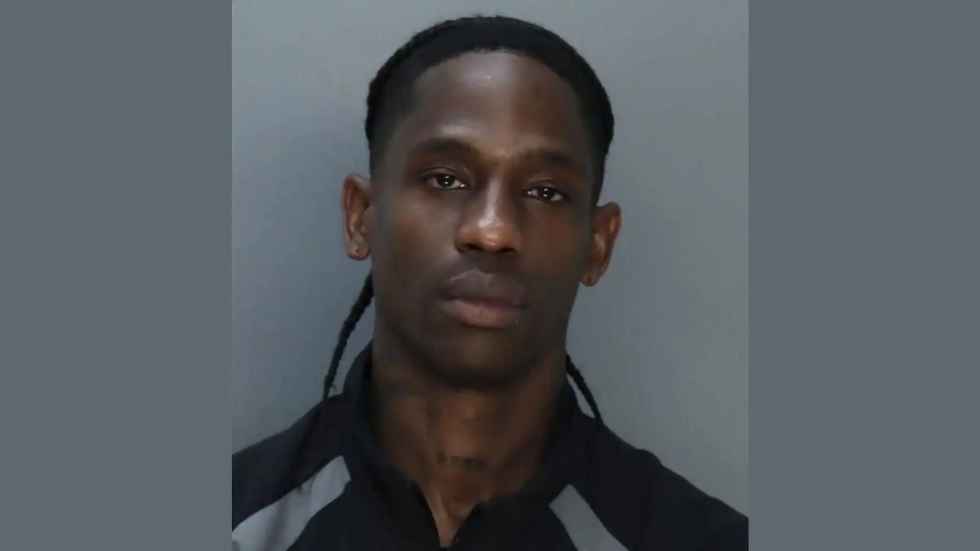 A man with long braids and a serious expression is seen against a plain background, wearing a dark shirt with light gray accents, resembling the stern ambiance of the Miami Beach Marina.