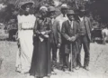 A group of seven people dressed in early 20th century attire stand outdoors, with four men wearing suits and hats, and three women in long dresses and hats, posing for a photo during one of the community events that celebrated Black culture.
