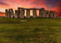 Stonehenge monument at sunset, with large standing stones arranged in a circular formation under a vibrant, colorful sky. Nearby, the ongoing Stonehenge road tunnel project has sparked numerous protests.