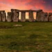 Stonehenge monument at sunset, with large standing stones arranged in a circular formation under a vibrant, colorful sky. Nearby, the ongoing Stonehenge road tunnel project has sparked numerous protests.