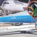 Three airplanes from Air France, KLM, and Delta Air Lines on a tarmac. Inset images include the Olympic rings against a stadium and the Eiffel Tower. Summer tourism is expected to soar, but some travelers might avoid Paris Olympics crowds by opting for alternative destinations.