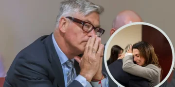 Alec Baldwin in a suit is seated, hands raised to his face in contemplation. Inset shows two people embracing, suggesting a moment of emotional support following the tragic Rust shooting.