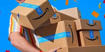 A person wearing a striped shirt carries several Amazon boxes with Prime Day tape against a blue background with colorful confetti, showcasing unmissable deals.