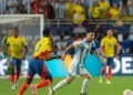 lionel messi in a blue and white striped Argentina jersey runs with the ball while a player in a yellow and blue Colombia jersey attempts to block his path during the Copa América Final 2024, with more players and spectators in the background.