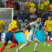 lionel messi in a blue and white striped Argentina jersey runs with the ball while a player in a yellow and blue Colombia jersey attempts to block his path during the Copa América Final 2024, with more players and spectators in the background.