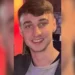 A young man with short brown hair and a gray shirt smiles at the camera against a blurred indoor background with red and yellow tones. The resemblance to missing British teenager Jay Slater, last seen in Tenerife, is striking.