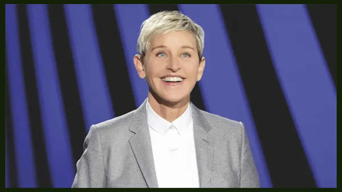 Ellen DeGeneres with short blonde hair wearing a grey blazer and white shirt, smiling against a blue and black striped background, reminiscent of Ellen DeGeneres promoting her Netflix special.
