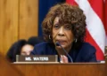 Maxine Waters with curly hair sits at a desk with a nameplate reading "Ms. Waters," speaking into a microphone, with a U.S. flag in the background. It appears to be an interview for CNN, featuring Congresswoman Maxine Waters.