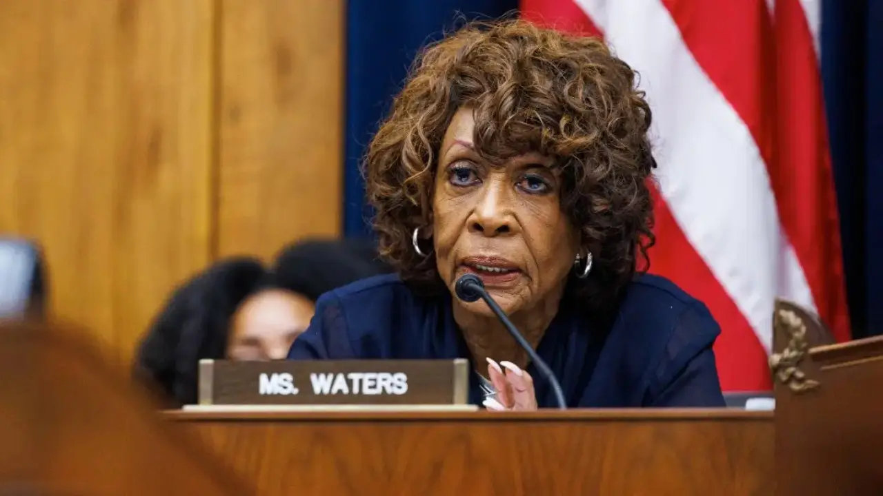 Maxine Waters with curly hair sits at a desk with a nameplate reading "Ms. Waters," speaking into a microphone, with a U.S. flag in the background. It appears to be an interview for CNN, featuring Congresswoman Maxine Waters.