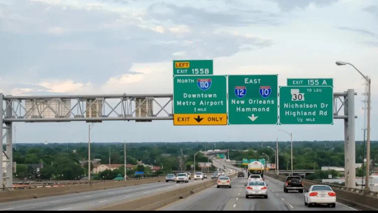 Multiple-lane highway with green overhead signs indicating exits 155B for I-110 North, and 155A for I-10 East towards New Orleans/Hammond, and LA-30 to Nicholson Dr/Highland Rd with cars driving below on a Louisiana highway.