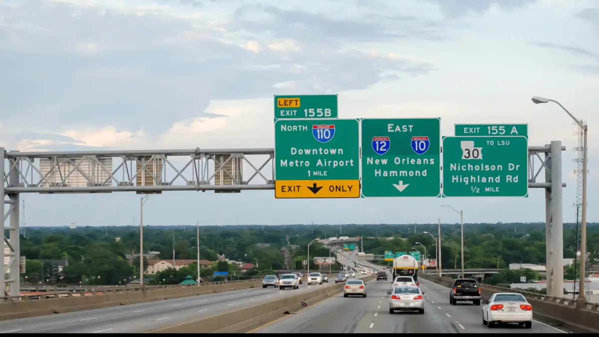 Multiple-lane highway with green overhead signs indicating exits 155B for I-110 North, and 155A for I-10 East towards New Orleans/Hammond, and LA-30 to Nicholson Dr/Highland Rd with cars driving below on a Louisiana highway.